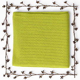 Folded yellow-green baby blanket with a fine striped texture, framed by decorative berry branches.