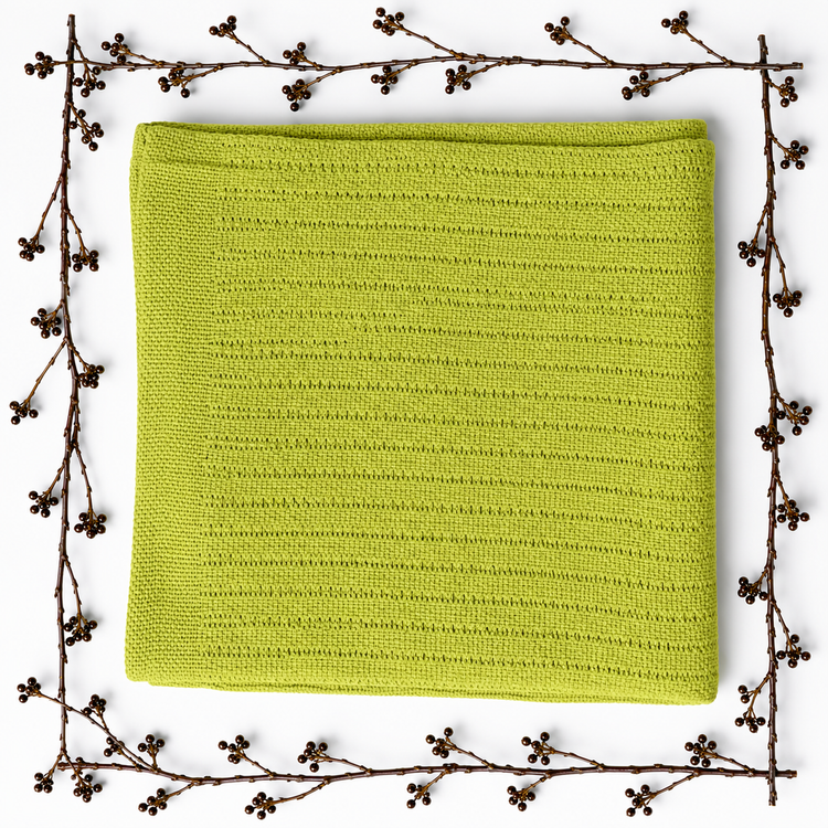 Folded yellow-green baby blanket with a fine striped texture, framed by decorative berry branches.