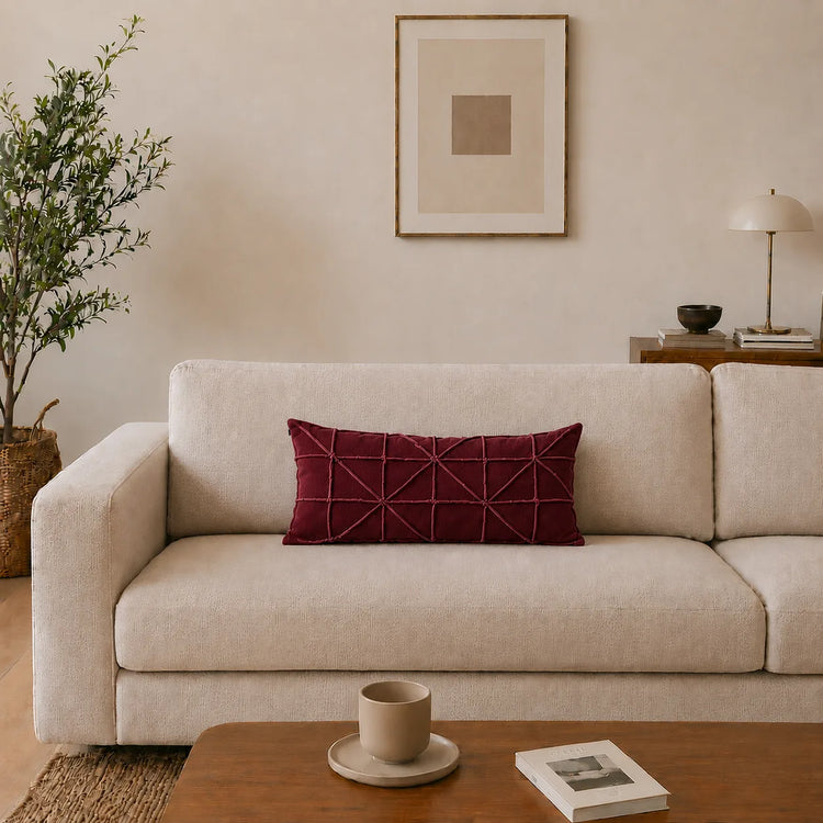 Rectangular burgundy filled cushion with intersecting geometric stitching on a cream sofa.