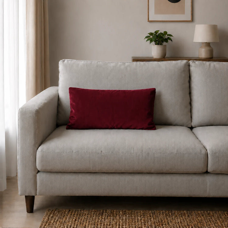 Plain rectangular burgundy filled cushion on a pale sofa.