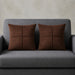 Two rust brown cushion covers with geometric panel stitching on a grey sofa.