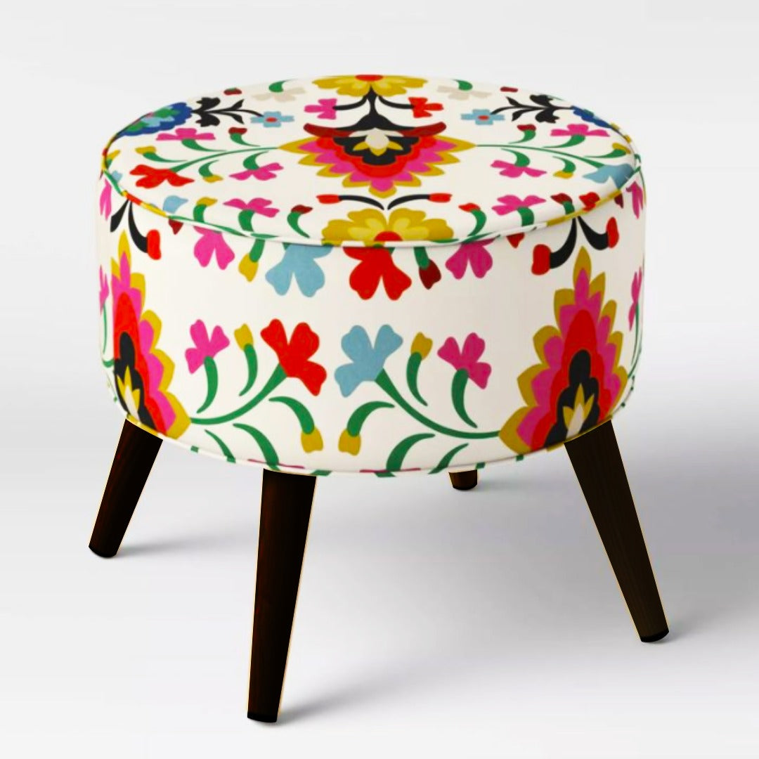 Round white ottoman with colourful floral upholstery and dark tapered legs.