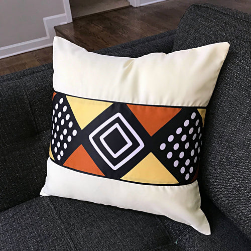 Cream cushion cover with a horizontal band of black, orange and yellow geometric shapes.