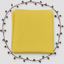 Folded yellow baby blanket with a waffle texture and plain border, surrounded by decorative berry branches.