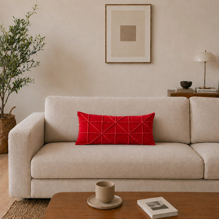 Rectangular red filled cushion with intersecting geometric stitching on a cream sofa.