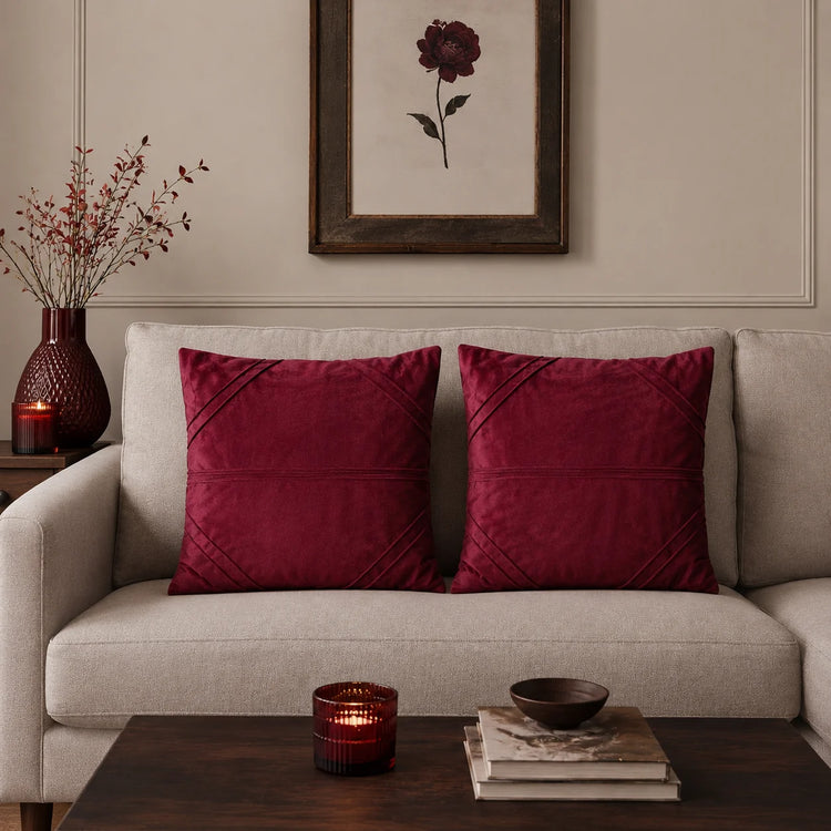 Two burgundy cushion covers with fine horizontal stitched lines on a beige sofa.