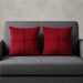Two red cushion covers with geometric panel stitching on a grey sofa.