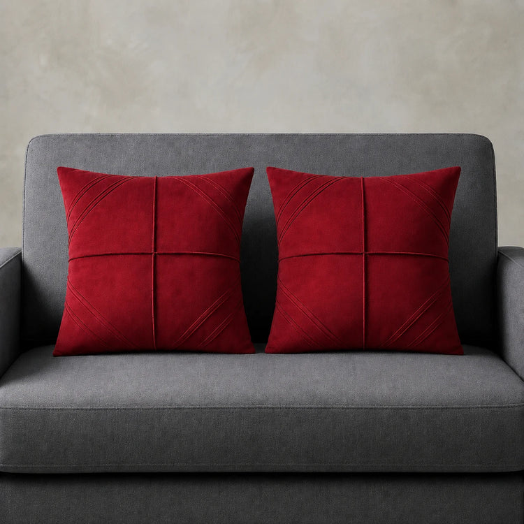 Two red cushion covers with geometric panel stitching on a grey sofa.