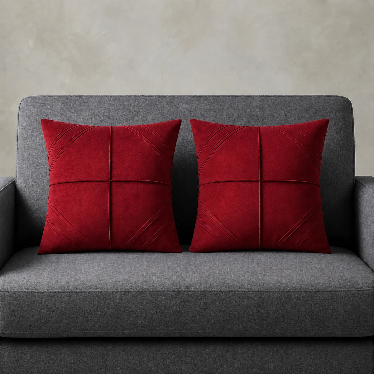Two red cushion covers with geometric panel stitching on a grey sofa.