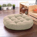 Round cream tufted floor cushion on a wooden floor.