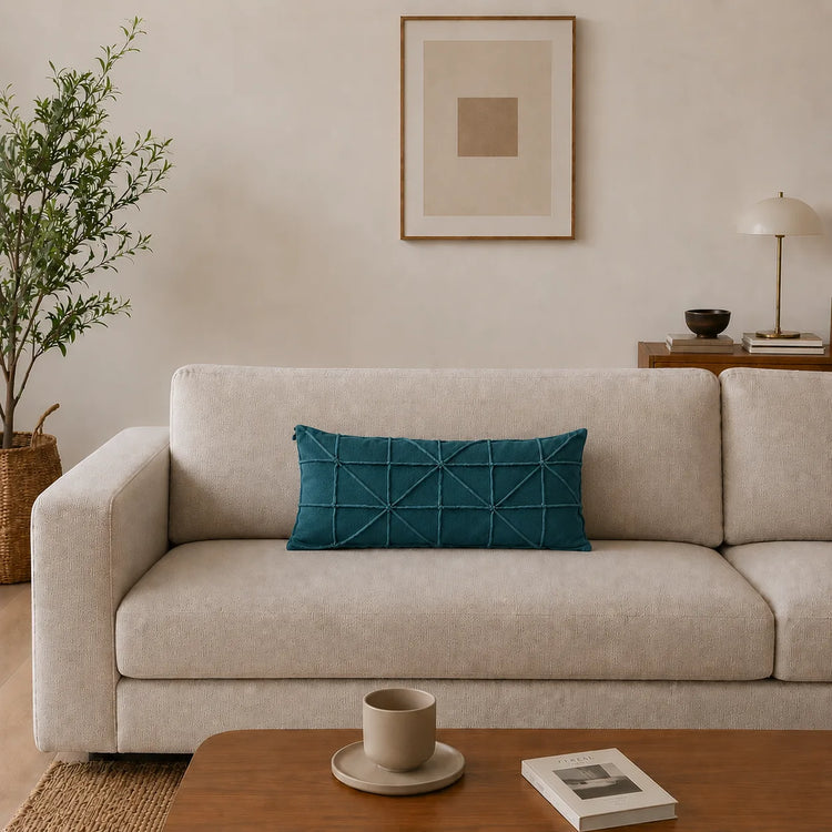 Rectangular teal filled cushion with intersecting geometric stitching on a cream sofa.