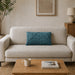 Rectangular teal filled cushion with angular stitched lines on a cream sofa.