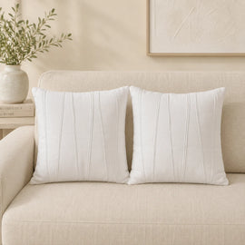Two white cushion covers with fine vertical stitched details on a cream sofa.