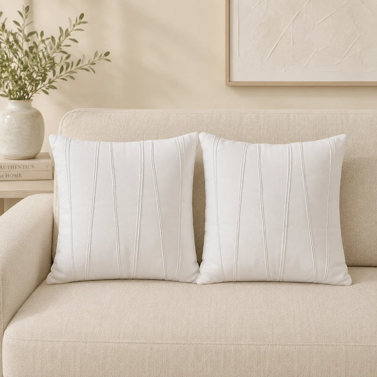 Two white cushion covers with fine vertical stitched details on a cream sofa.