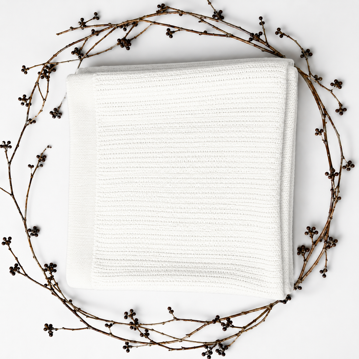 Folded white ribbed blanket framed by decorative dried branches.