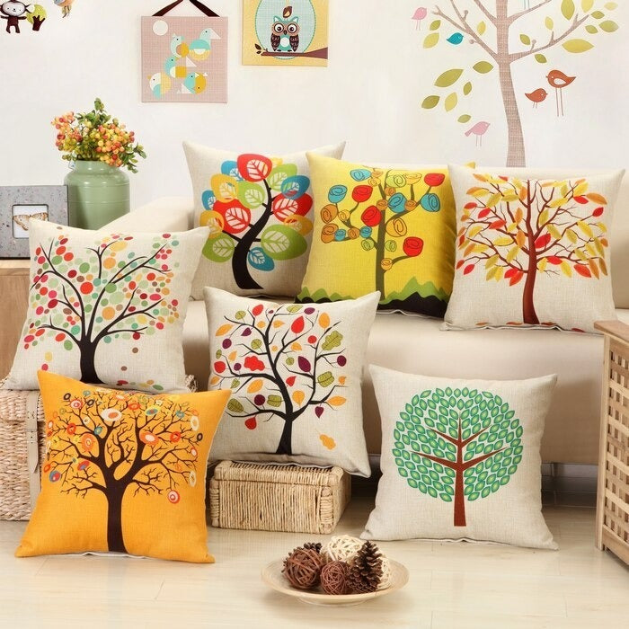 Cushion covers with colourful tree prints arranged on a cream sofa and floor.