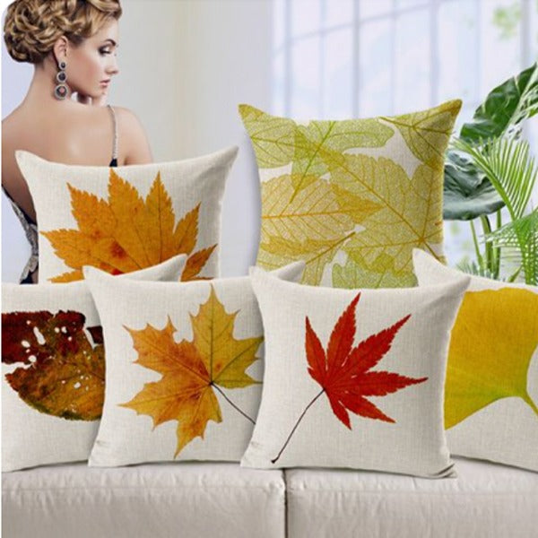 Cream cushion covers with colourful autumn leaf prints arranged on a sofa.