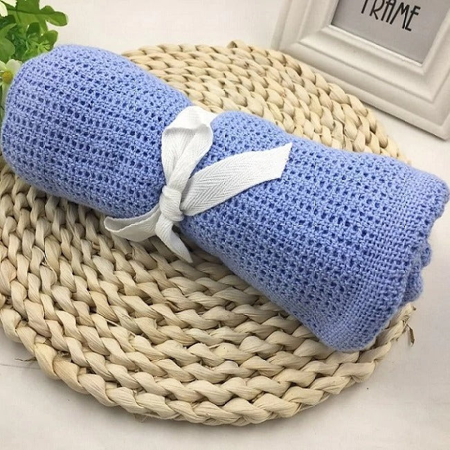 Rolled blue cellular blanket tied with a white ribbon on a woven mat.