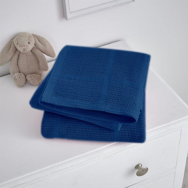 Folded navy blue cellular blanket on a white cabinet beside a plush rabbit.