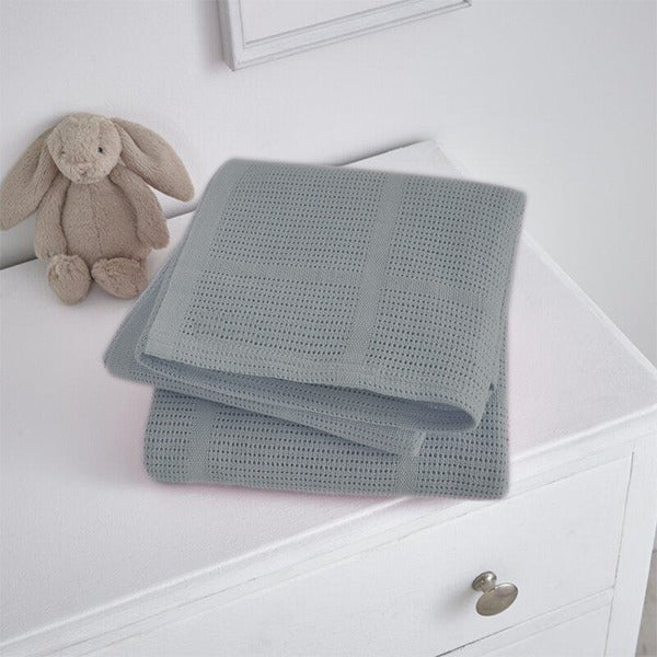 Folded grey cellular blanket on a white cabinet beside a plush rabbit.