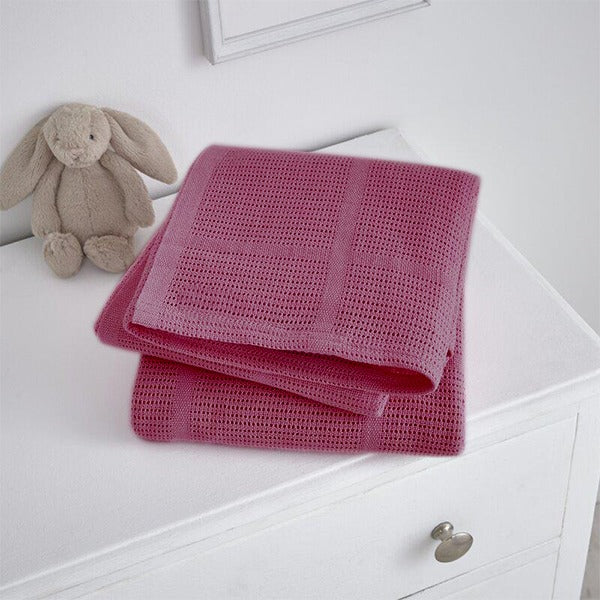 Folded magenta cellular blanket on a white cabinet beside a plush rabbit.