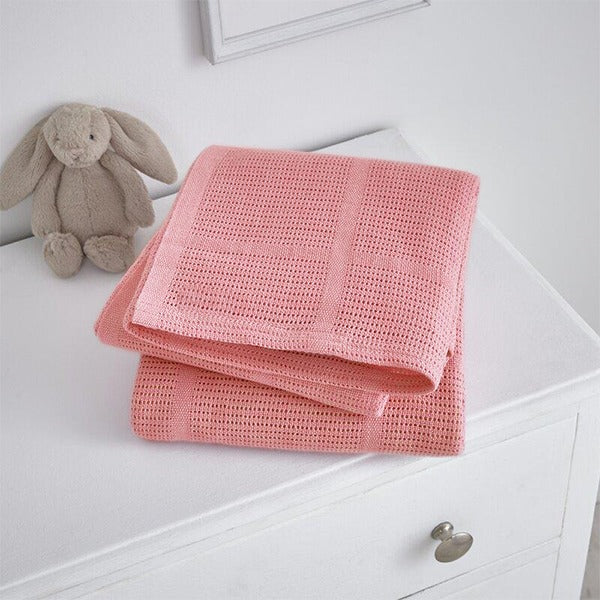 Folded coral pink cellular blanket on a white cabinet beside a plush rabbit.