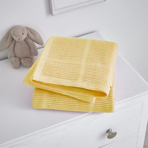 Folded yellow cellular blanket on a white cabinet beside a plush rabbit.