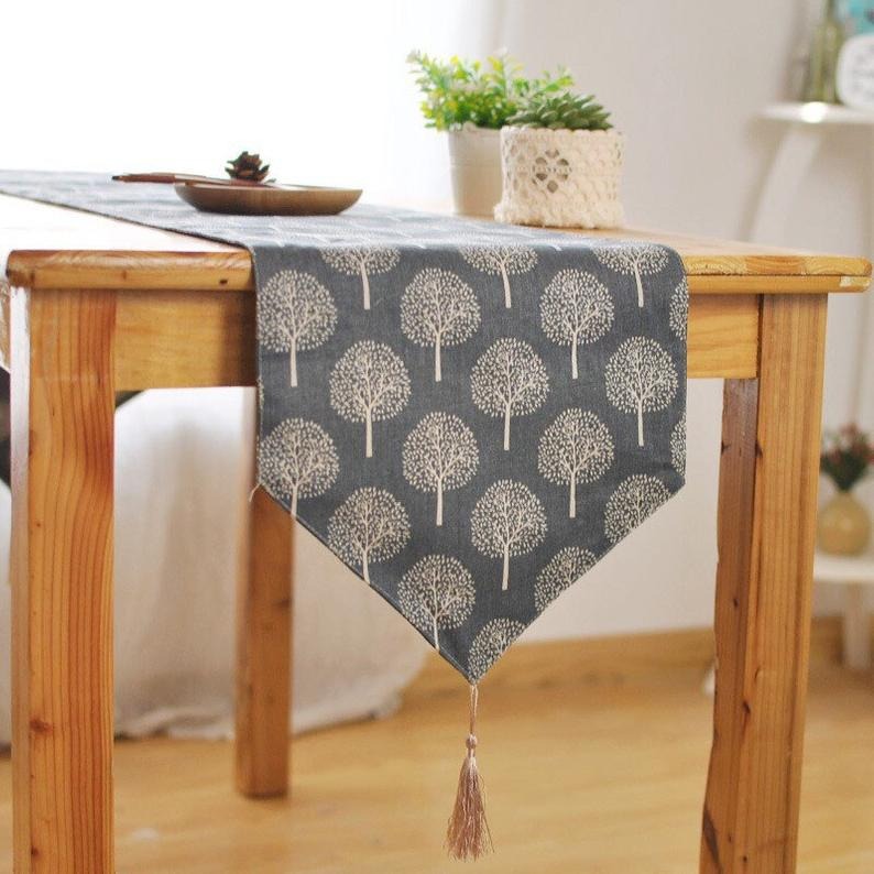 Grey table runner with light tree motifs and a tasselled end.