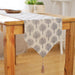 Light beige table runner with grey tree motifs and a tasselled end.