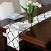 White table runner with black curved trellis lines on a dark dining table.