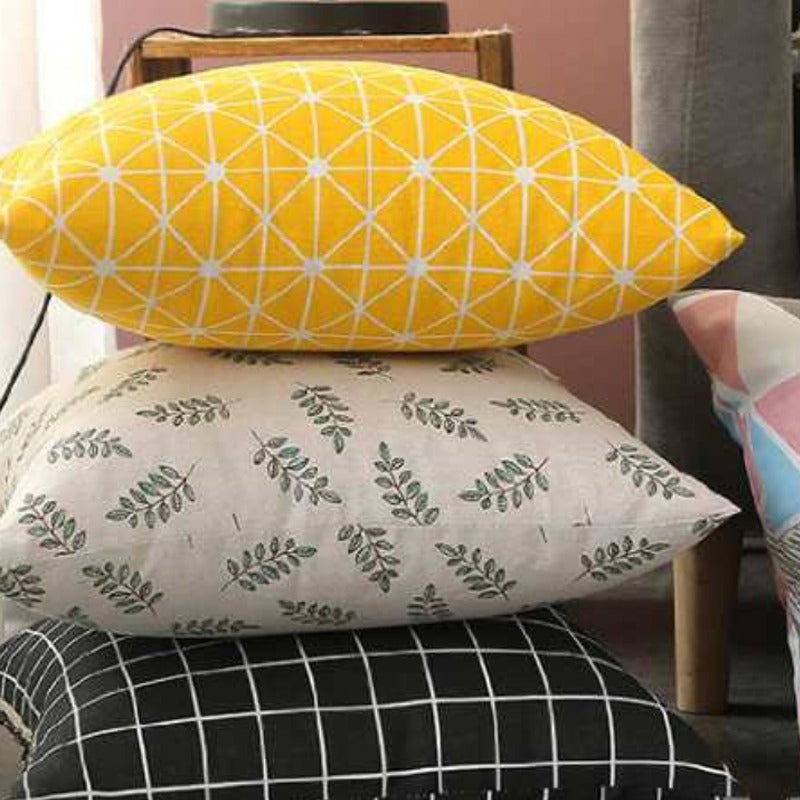 Close view of stacked cushion covers with yellow triangles, green leaves and dark geometric patterns.