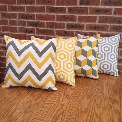 Four yellow, grey and white cushion covers with zigzag, cube and hexagon patterns.
