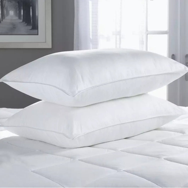 Two white fibre-filled pillows stacked on a mattress.