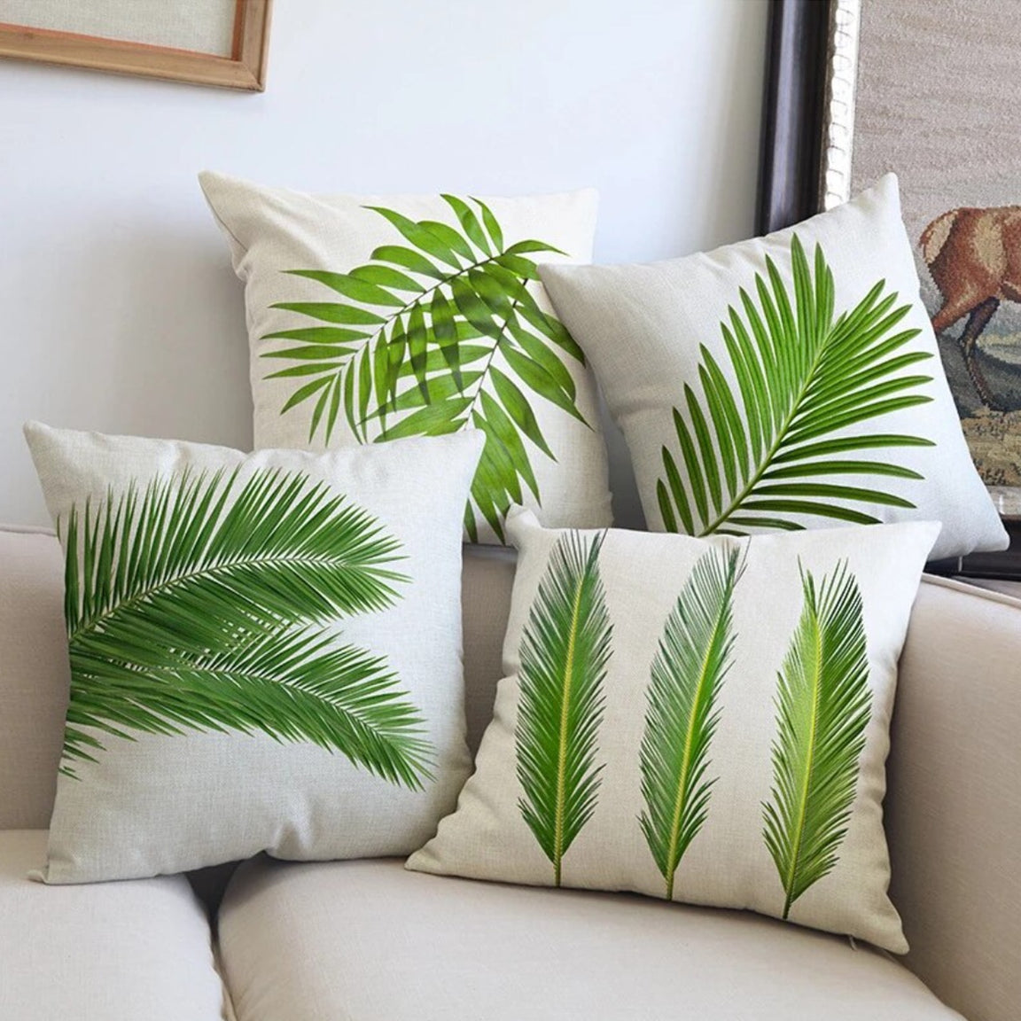 White cushion covers with assorted green tropical leaf prints arranged on a sofa.