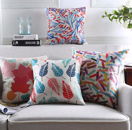 Four colourful printed cushion covers displayed on a grey sofa.