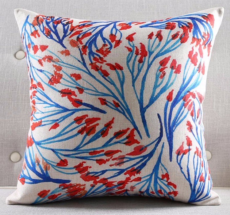 White cushion cover with swirling blue branches and small red leaves.