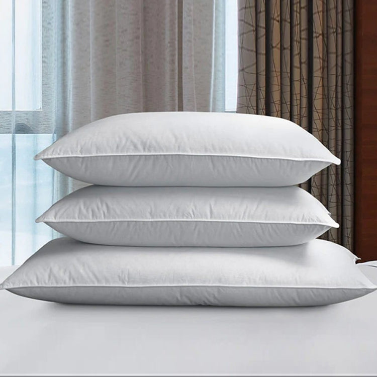 Three white fibre-filled pillows stacked on a bed.