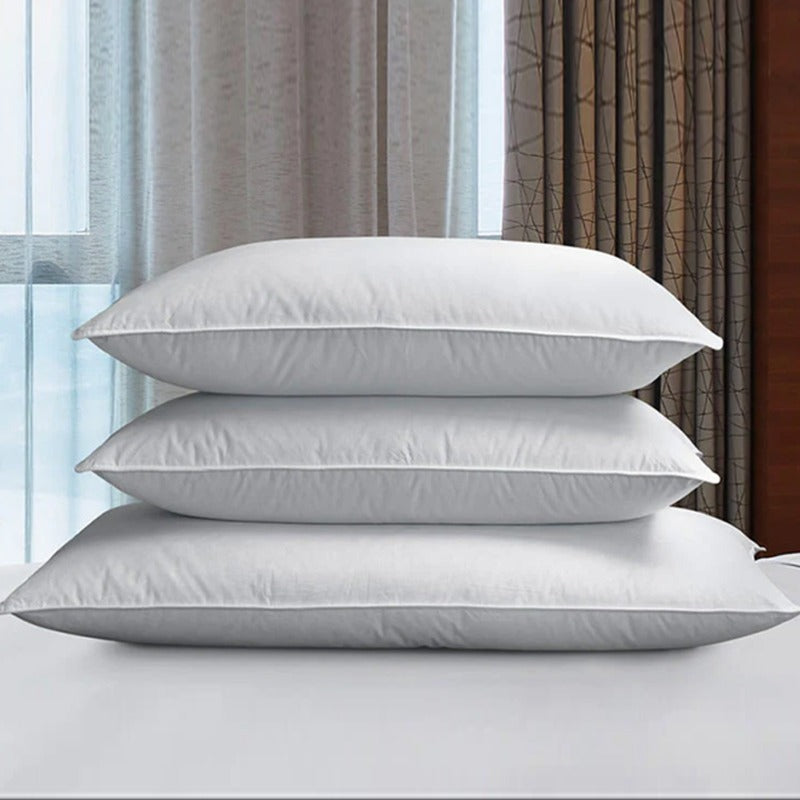 Three white fibre-filled pillows stacked on a bed.