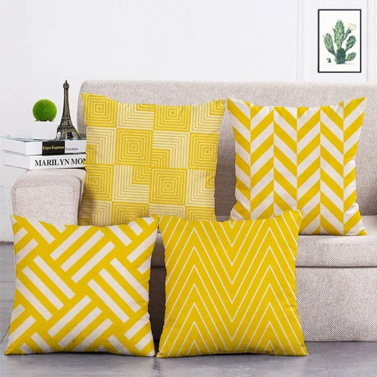 Four yellow and white cushion covers with geometric patterns arranged on a light sofa.