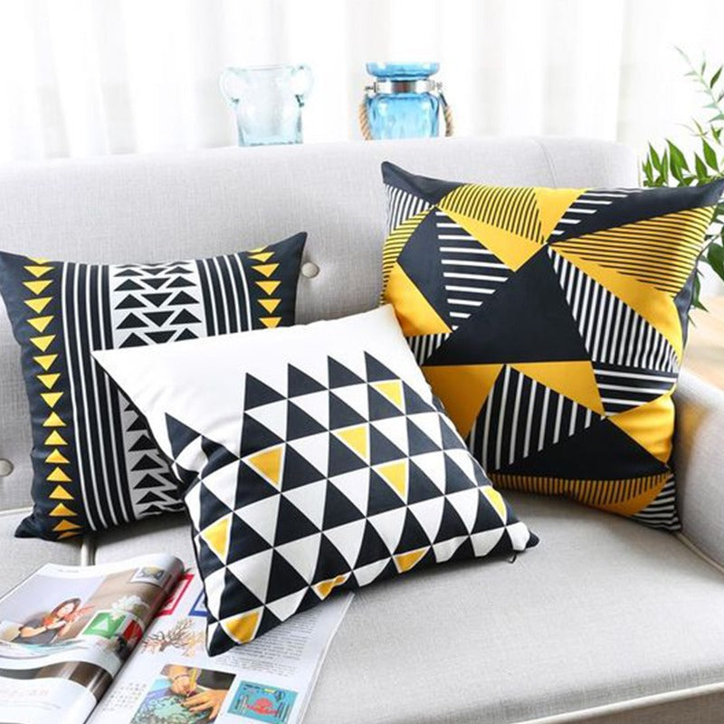 Three black, yellow and white geometric cushion covers arranged on a sofa.