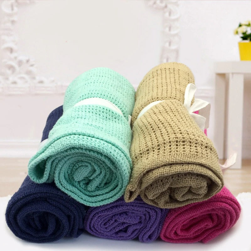 Five rolled cellular blankets in mint, beige, navy, purple and magenta, tied with white ribbons.