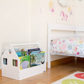 White house-shaped book storage bin filled with children's books beside a bed.