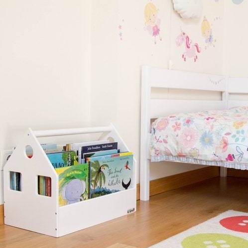 White house-shaped book storage bin filled with children's books beside a bed.