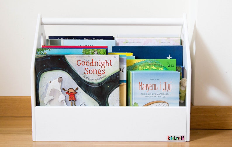 Front view of a white house-shaped book bin with several children's books on display.