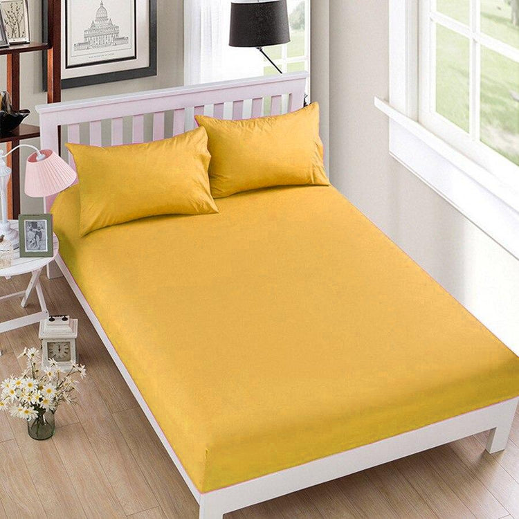 Ochre cotton fitted sheet displayed on a bed with matching pillowcases.